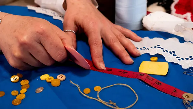 Hands measuring fabric beside a spread of yellow buttons and thread