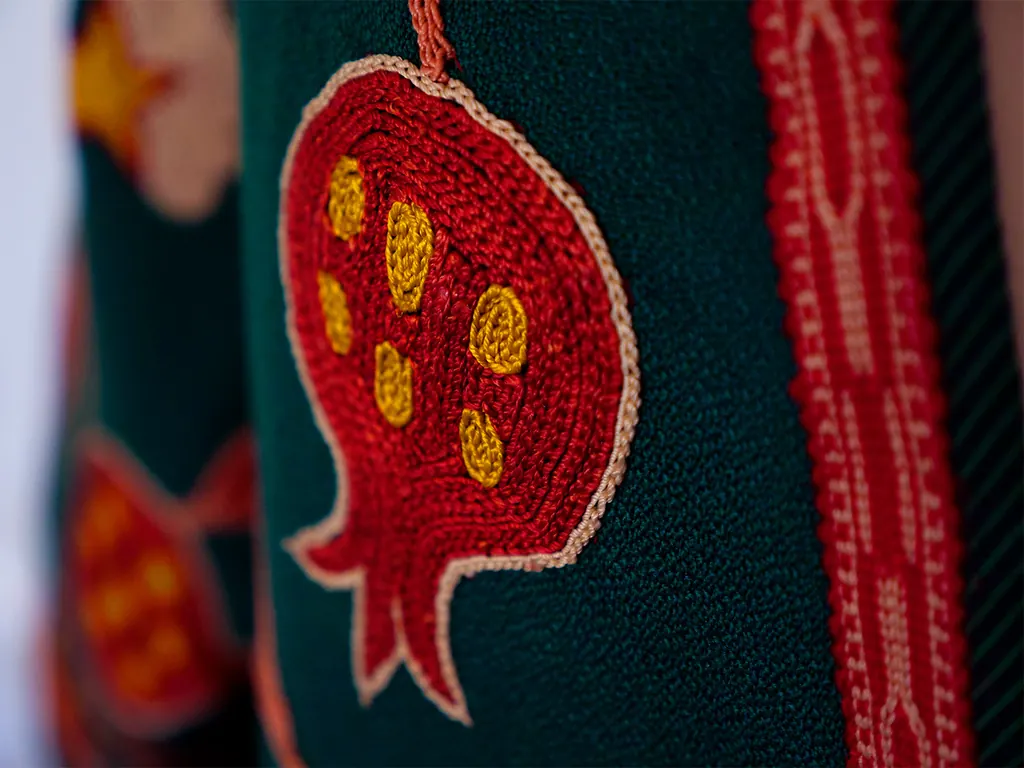 Close-up of red pomegranate embroidery stitched on green cloth
