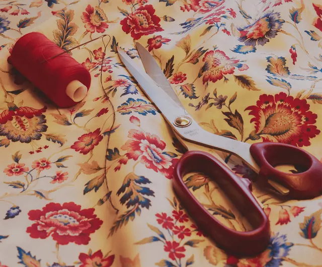 Tailor's scissors and a spool of thread resting on floral fabric