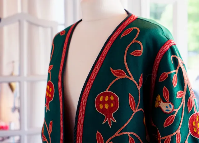 A green jacket with red pomegranate embroidery on a mannequin